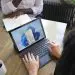 Overhead view of two people at a table working with a Microsoft laptop and notebook